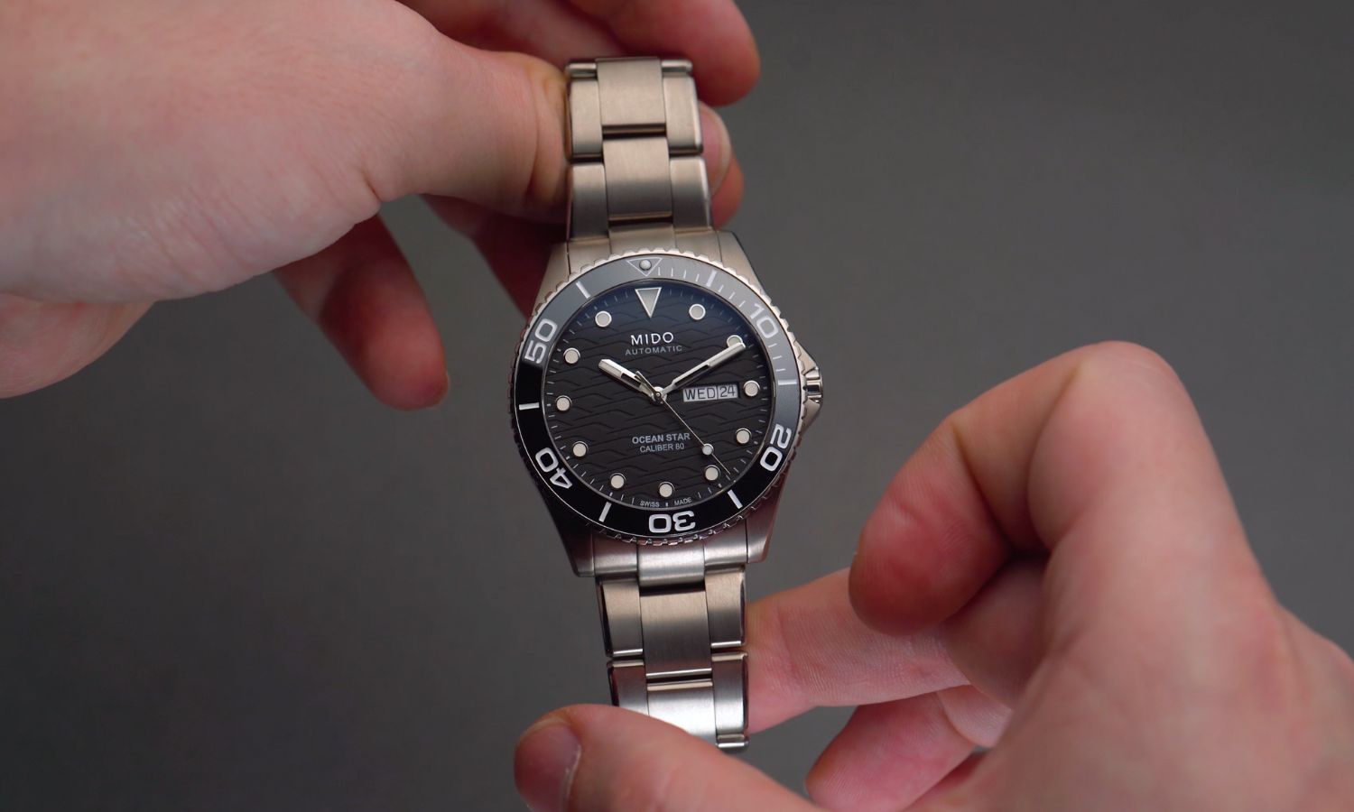 Mido Ocean Star 200 C Titan mit schwarzem Zifferblatt am Titanarmband in zwei Händen gehalten vor grauem Hintergrund