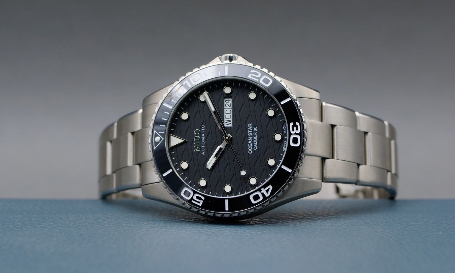 Mido Ocean Star 200 C Titan mit schwarzem Zifferblatt am Titanarmband auf der Seite liegend vor grauem Hintergrund
