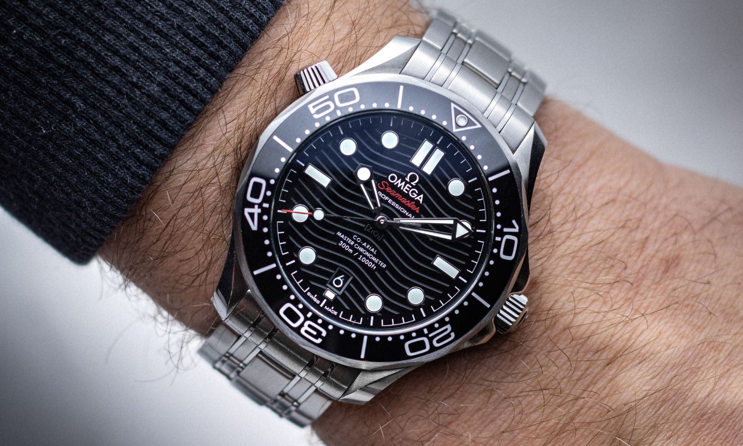 OMEGA Seamaster Diver 300M 42 mit schwarzem Zifferblatt am Edelstahlarmband an einem Handgelenk mit schwarzem Ärmel getragen vor hellem Hintergrund