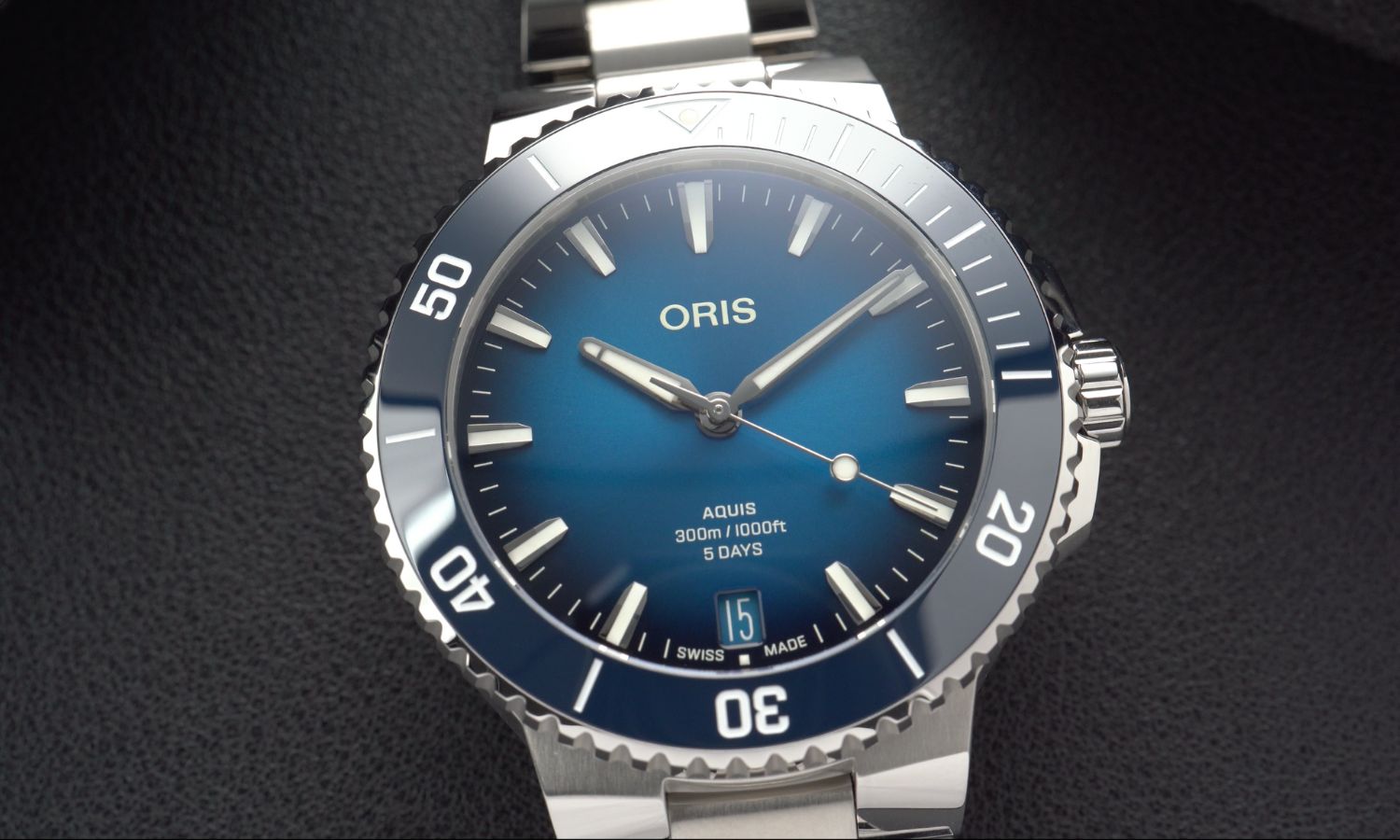 Nahaufnahme der Oris Aquis Date Calibre 400 mit blauem Zifferblatt am Edelstahlarmband liegend vor dunkelgrauem Hintergrund