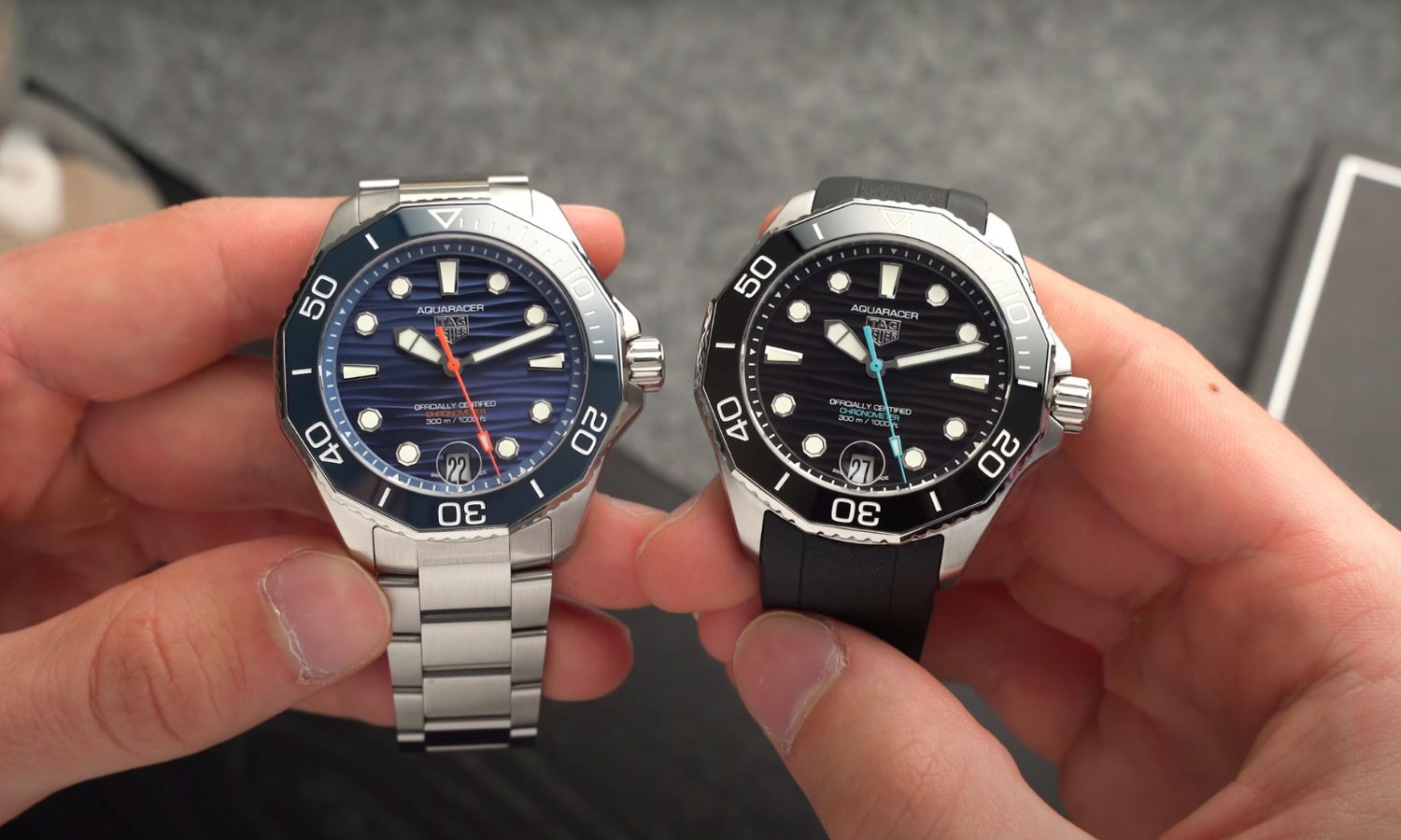 TAG HEUER Aquaracer Professional 300 Date mit blauem Zifferblatt am Edelstahlarmband links und mit schwarzem Zifferblatt am schwarzen Kautschukarmband rechts in zwei Händen gehalten vor hellgrauem Hintergrund