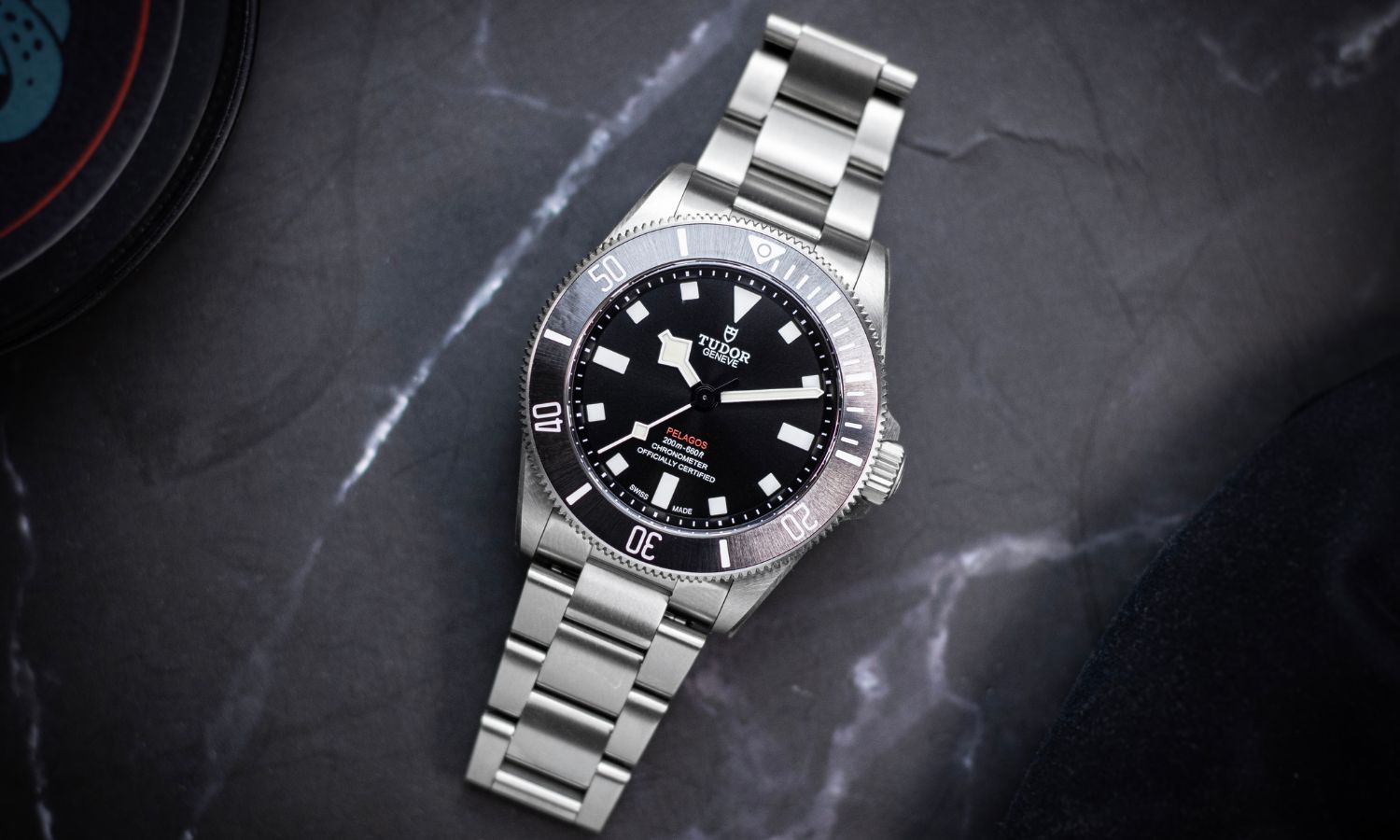 TUDOR Pelagos 39 mit schwarzem Zifferblatt am Edelstahlarmband liegend vor dunkelgrauem Hintergrund