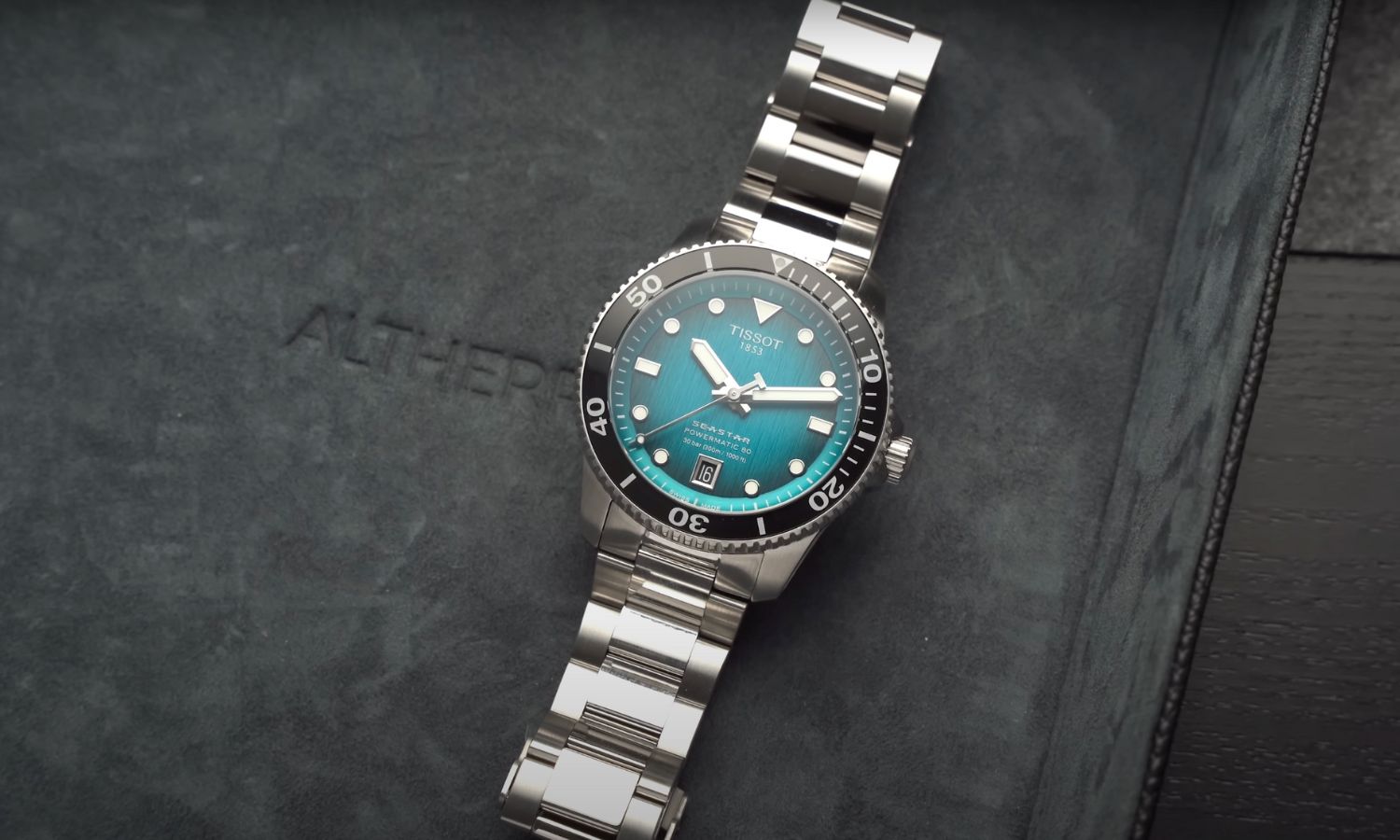 Tissot Seastar 1000 Powermatic 80 40 mm mit türkisem Zifferblatt am Edelstahlarmband liegend vor dunkelgrauem Hintergrund