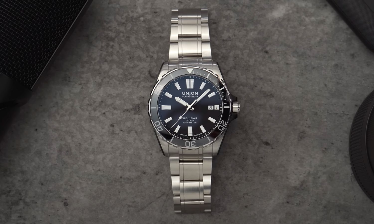 UNION Glashütte Belisar Datum Sport Pro mit schwarzem Zifferblatt am Edelstahlarmband liegend vor grauem Hintergrund