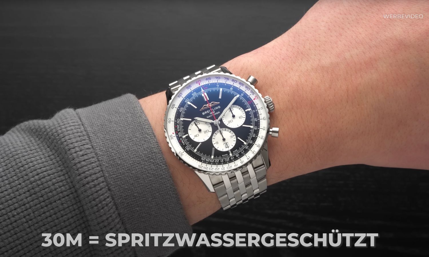 Breitling Navitimer mit schwarzem Zifferblatt am Edelstahlarmband an einem Handgelenk mit grauem Ärmel getragen vor schwarzem Hintergrund mit Angabe der Wasserdichtigkeit