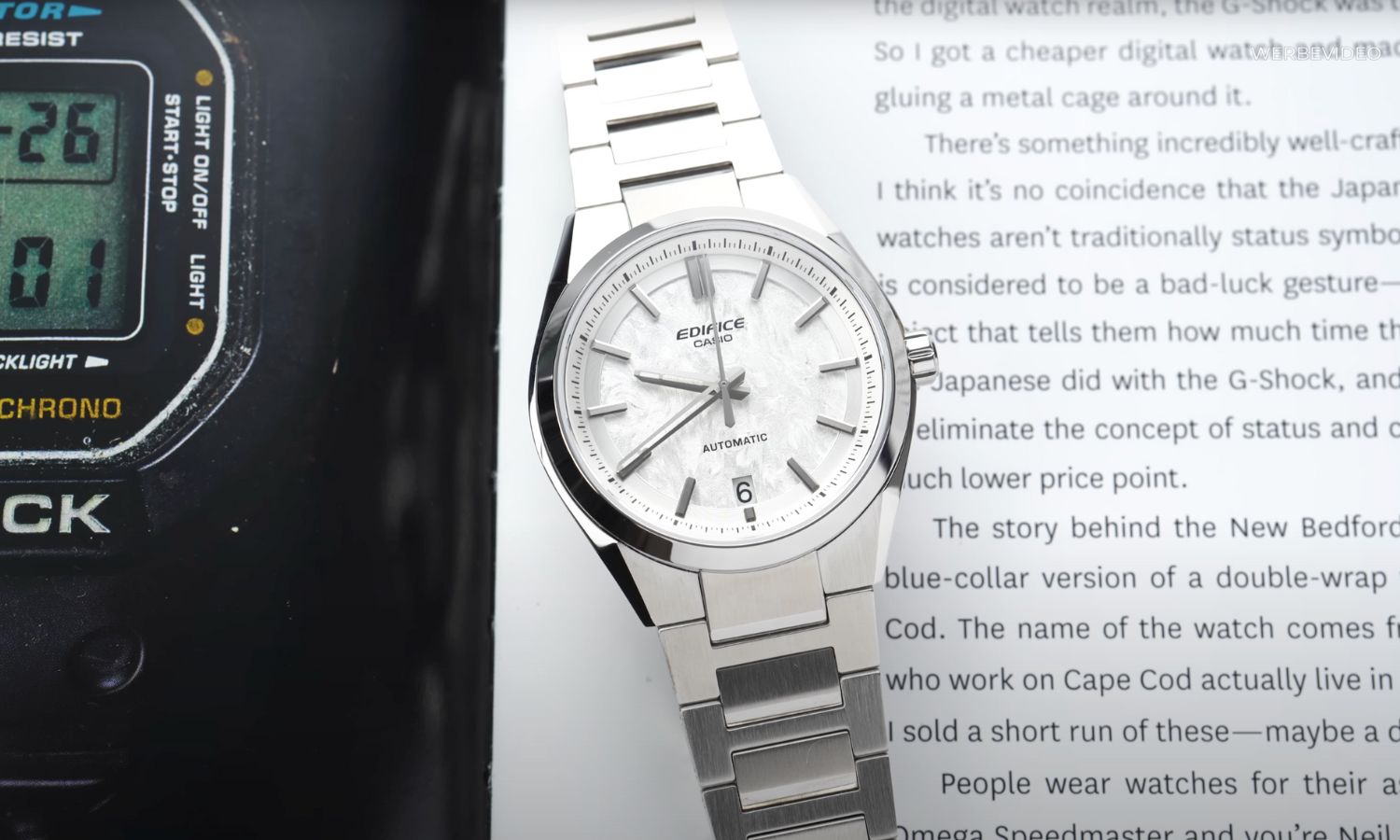 Casio Automatic EFK-100 mit weißem Zifferblatt am Edelstahlarmband liegend auf einem Buch mit weißen Seiten und schwarzer Schrift und einem Bild einer Casio G-Shock