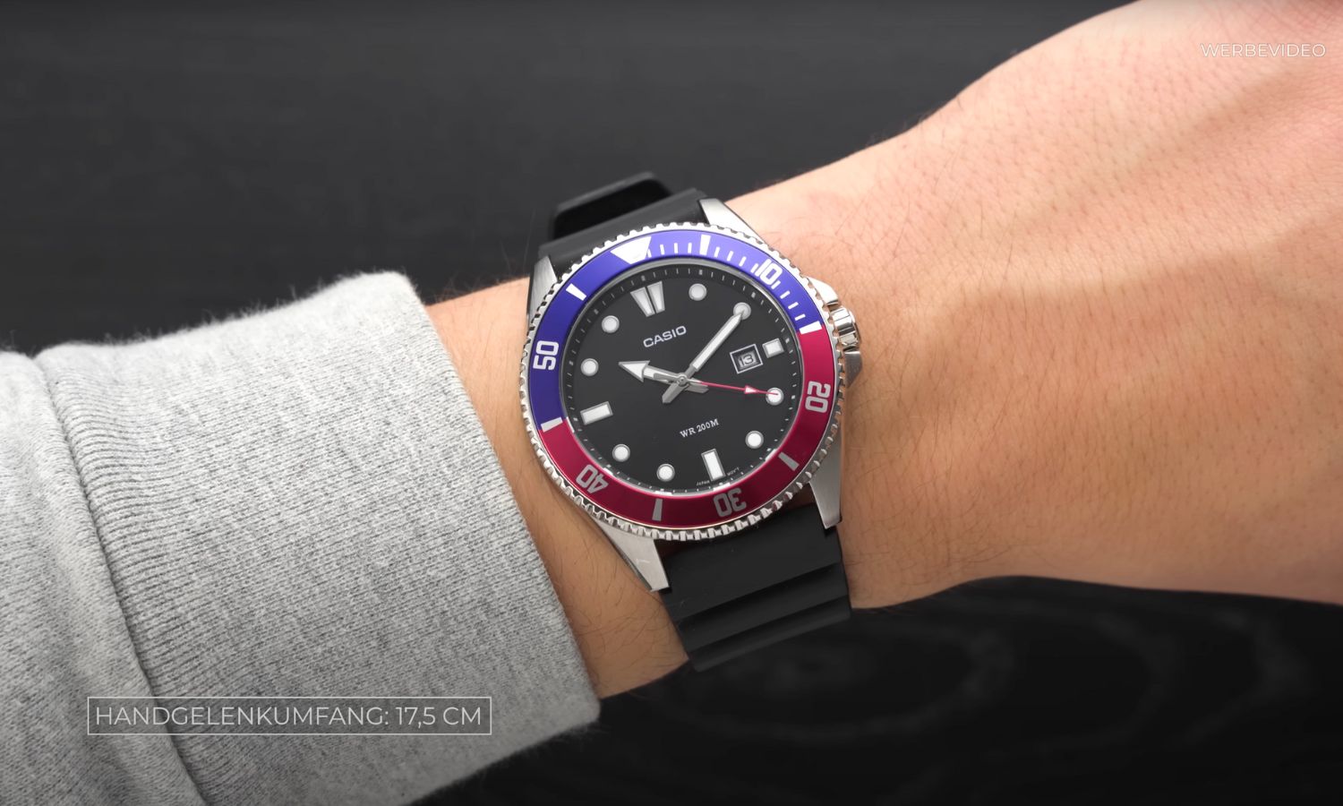 Casio Duro MDV-107-1A3V mit schwarzem Zifferblatt am schwarzen Kunststoffarmband an einem Handgelenk mit grauem Ärmel getragen vor schwarzem Hintergrund