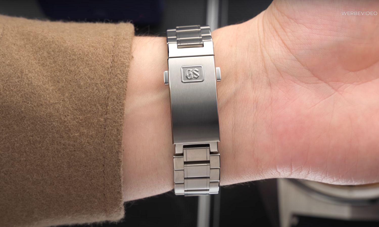Das Titanarmband und die Schließe der Grand Seiko Evolution 9 SLGB003 Ice Forest an einem Handgelenk mit braunem Ärmel getragen
