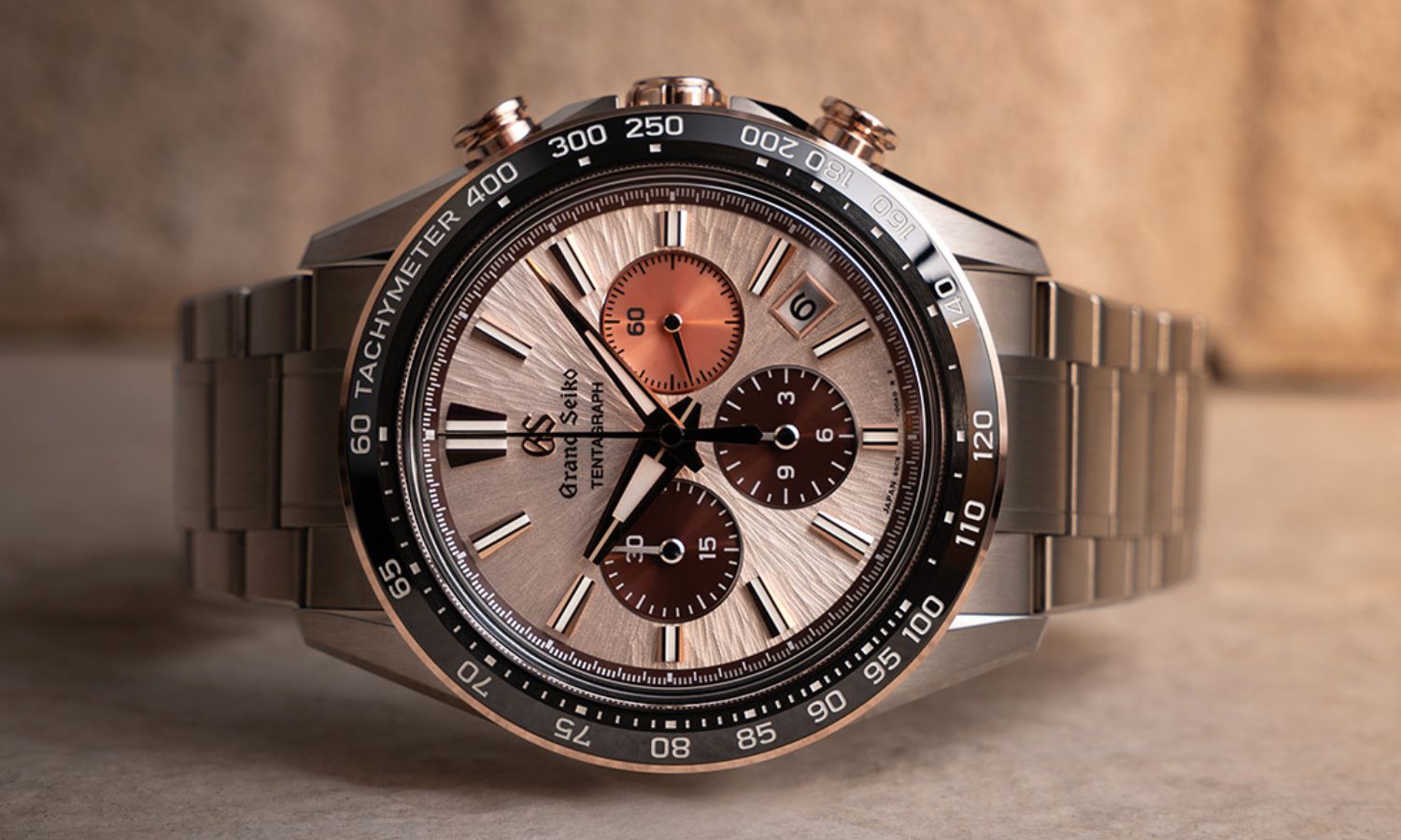 Grand Seiko SLGC006 Sunrise Tentagraph mit kupferfarbenem Zifferblatt am Edelstahlarmband auf der Seite liegend abgebildet vor leuchtendem Hintergrund
