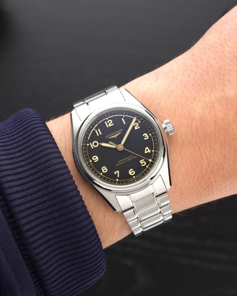 Longines Spirit Pilot Referenz L3.809.4.53.6 mit schwarzem Zifferblatt am Edelstahlarmband an einem Handgelenk mit dunkelblauem Ärmel getragen vor schwarzem Hintergrund