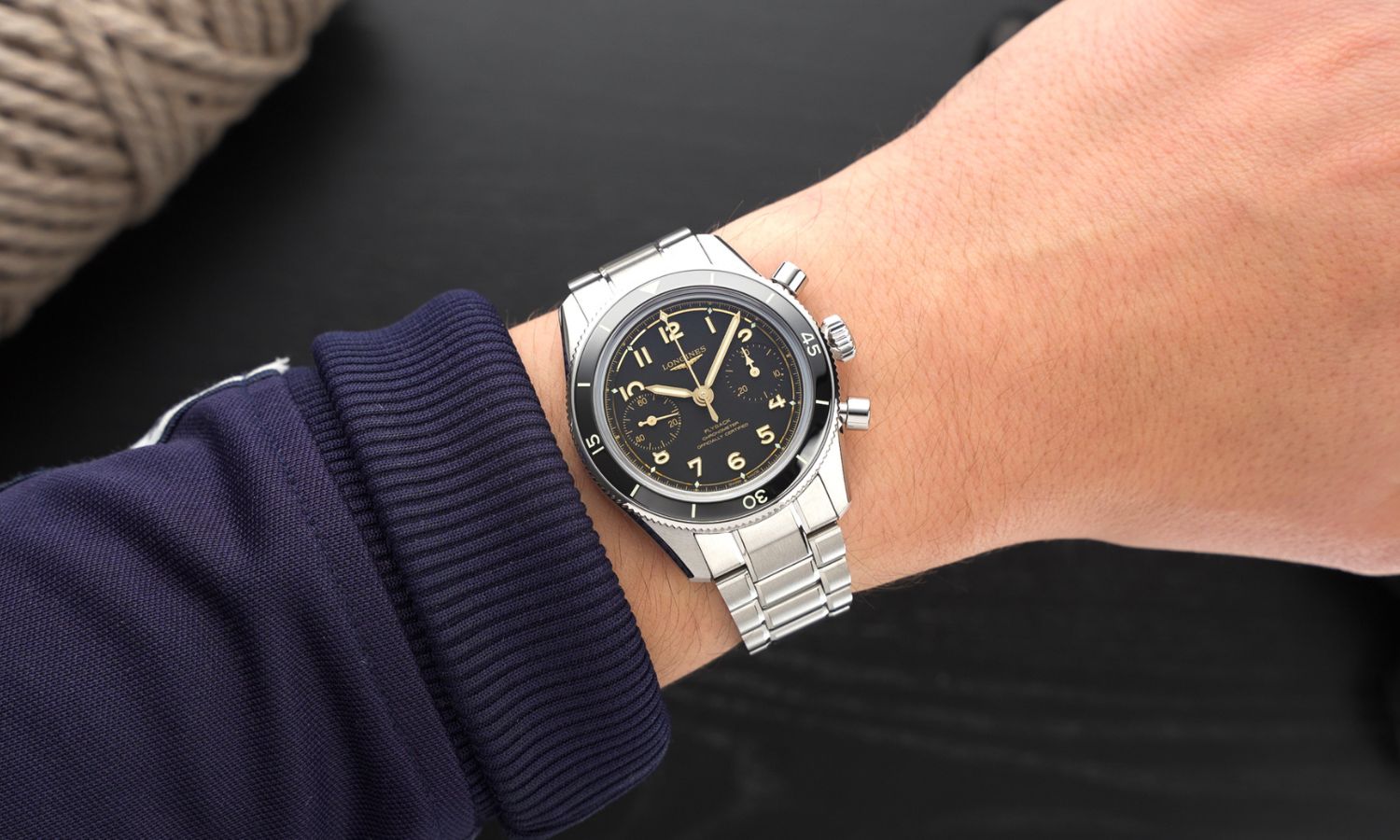 Longines Spirit Pilot Flyback Chronograph Referenz L3.721.4.53.6 mit schwarzem Zifferblatt am Edelstahlarmband an einem Handgelenk mit dunkelblauem Ärmel getragen vor schwarzem Hintergrund