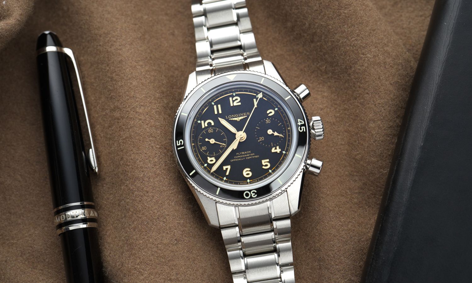 Longines Spirit Pilot Flyback Chronograph Referenz L3.721.4.53.6 mit schwarzem Zifferblatt am Edelstahlarmband von vorne abgebildet liegend neben einem schwarzen Kugelschreiber vor braunem Hintergrund