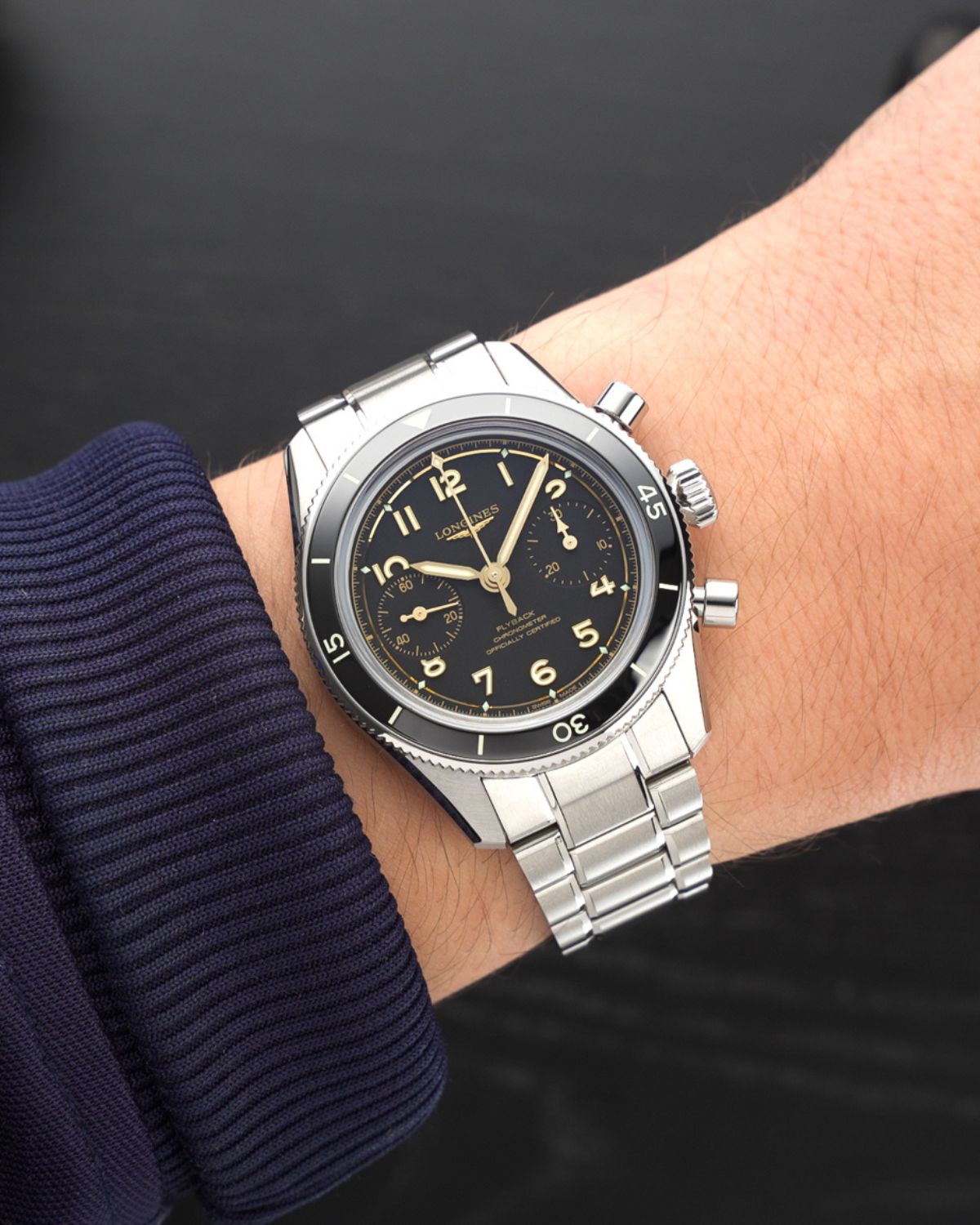 Longines Spirit Pilot Flyback Chronograph Referenz L3.721.4.53.6 mit schwarzem Zifferblatt am Edelstahlarmband an einem Handgelenk mit dunkelblauem Ärmel getragen vor schwarzem Hintergrund