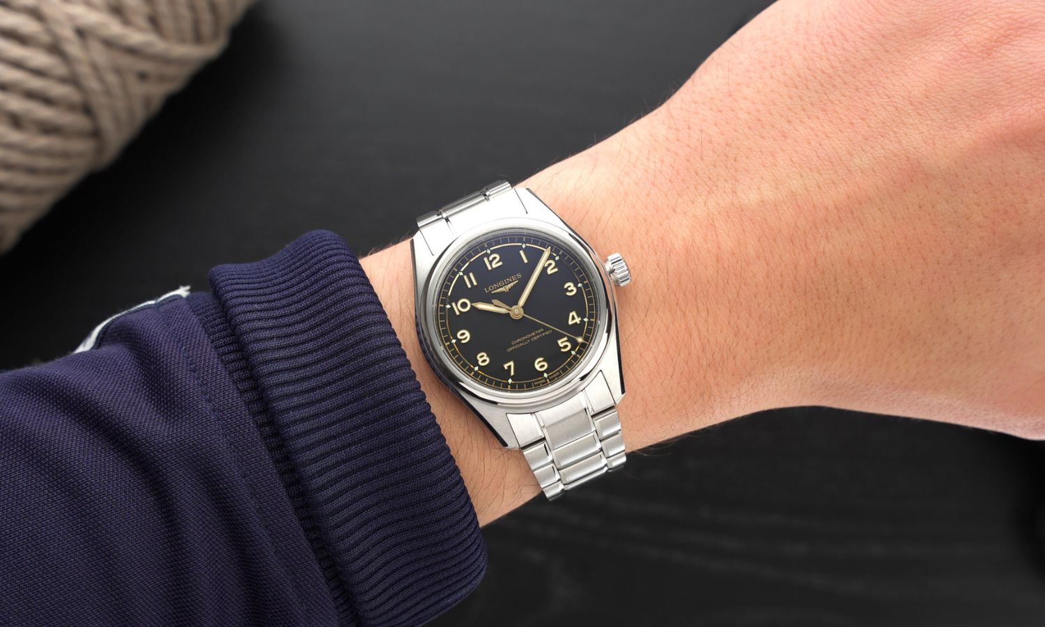 Longines Spirit Pilot Referenz L3.809.4.53.6 mit schwarzem Zifferblatt am Edelstahlarmband an einem Handgelenk mit dunkelblauem Ärmel getragen vor schwarzem Hintergrund