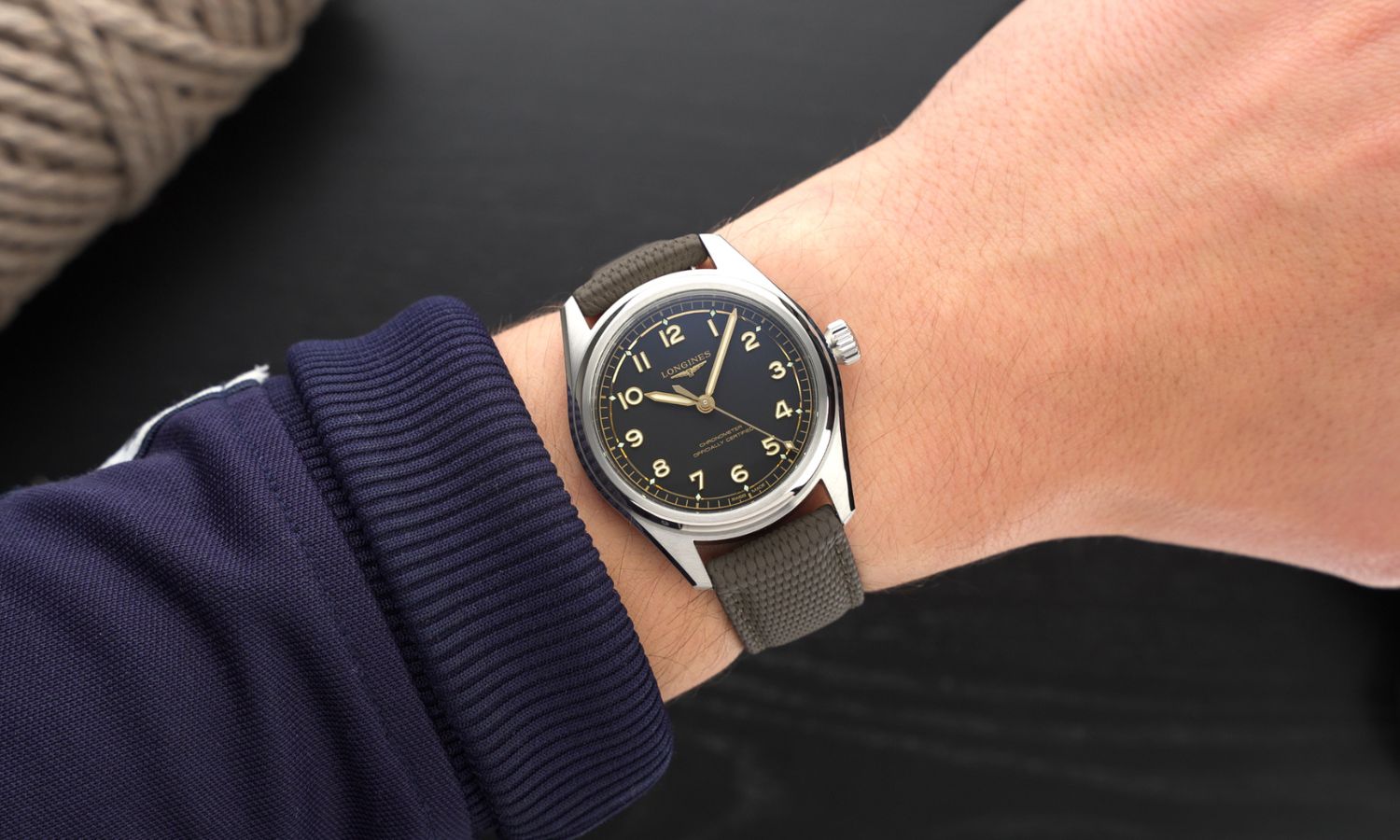 Longines Spirit Pilot Referenz L3.809.4.53.9 mit schwarzem Zifferblatt am grünen Kautschukarmband an einem Handgelenk mit dunkelblauem Ärmel getragen vor schwarzem Hintergrund
