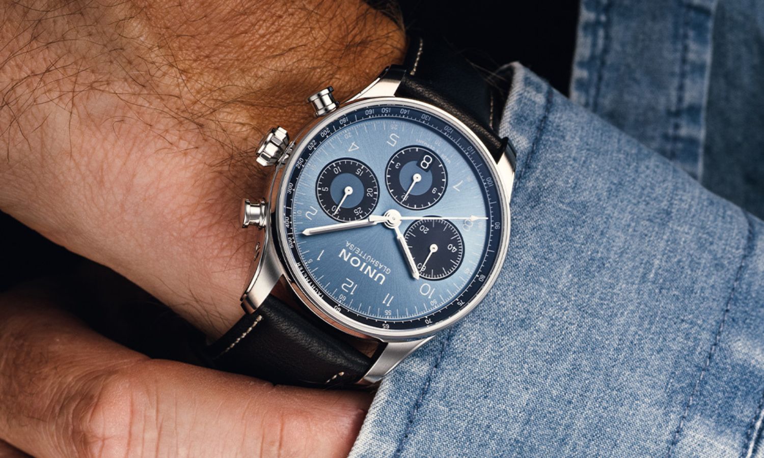 UNION Glashütte Belisar Chronograph Referenz D009.227.16.042.00 mit blauem Zifferblatt am schwarzen Kalbslederarmband an einem Handgelenk mit Jeansjacken-Ärmel getragen