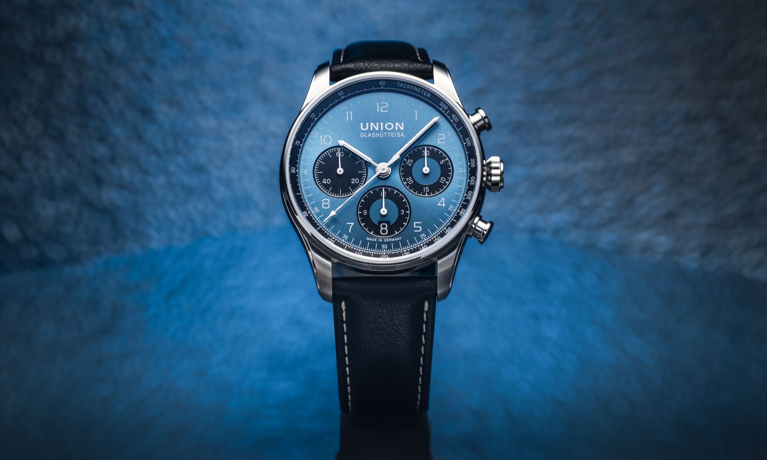 UNION Glashütte Belisar Chronograph Referenz D009.227.16.042.00 mit blauem Zifferblatt am schwarzen Kalbslederarmband stehend vor blauem Hintergrund