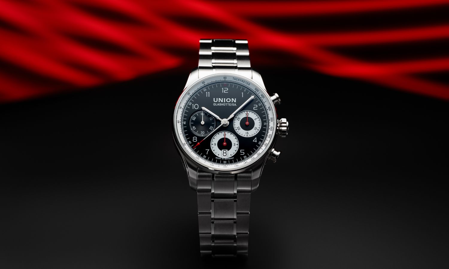 UNION Glashütte Belisar Chronograph Referenz D009.227.11.052.00 mit schwarzem Zifferblatt am Edelstahlarmband stehend vor rot schwarzem Hintergrund