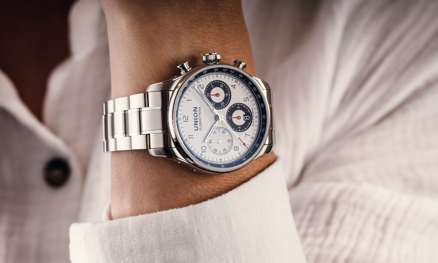 UNION Glashütte Belisar Chronograph Referenz D009.227.11.012.00 mit weißem Zifferblatt am Edelstahlarmband an einem Handgelenk mit weißem Ärmel getragen