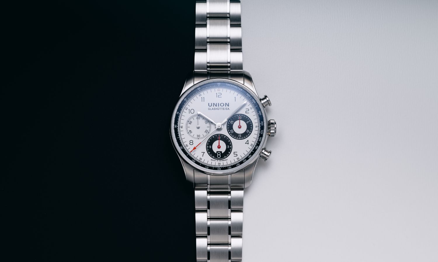 UNION Glashütte Belisar Chronograph Referenz D009.227.11.012.00 mit weißem Zifferblatt am Edelstahlarmband liegend vor schwarz weißem Hintergrund