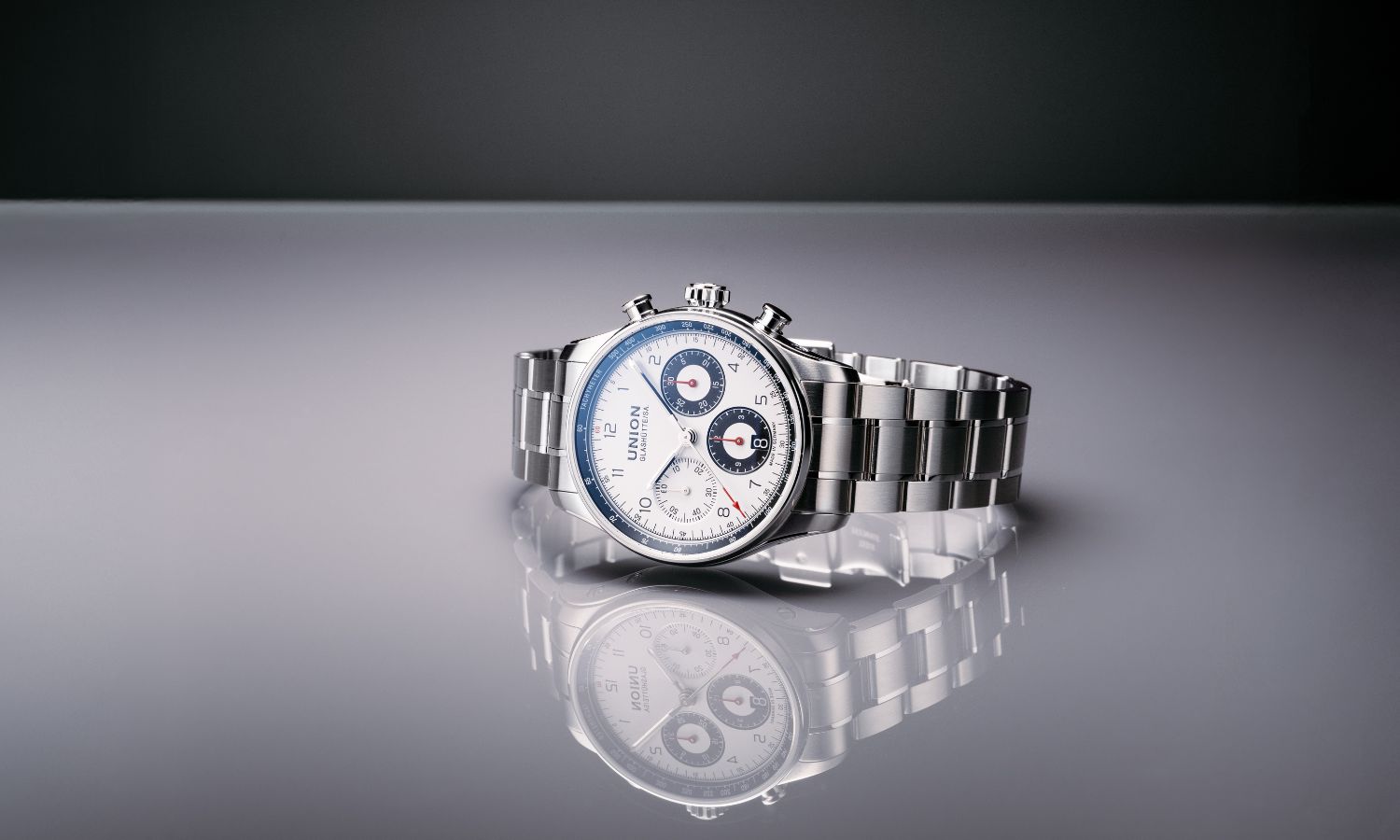 UNION Glashütte Belisar Chronograph Referenz D009.227.11.012.00 mit weißem Zifferblatt am Edelstahlarmband seitlich liegend vor grauem Hintergrund