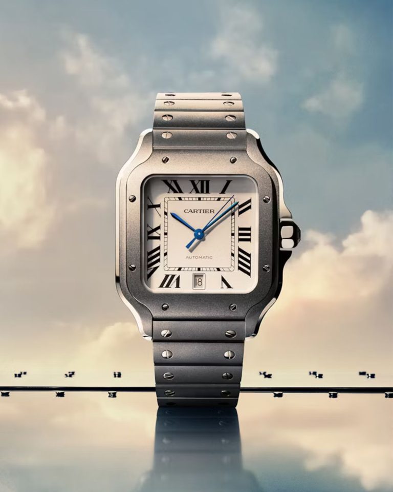 Cartier Santos Referenz WSSA0089 mit Titangehäuse, Titanarmband und weißem Zifferblatt stehend auf einem Metallboden vor blauem Himmel mit Wolken