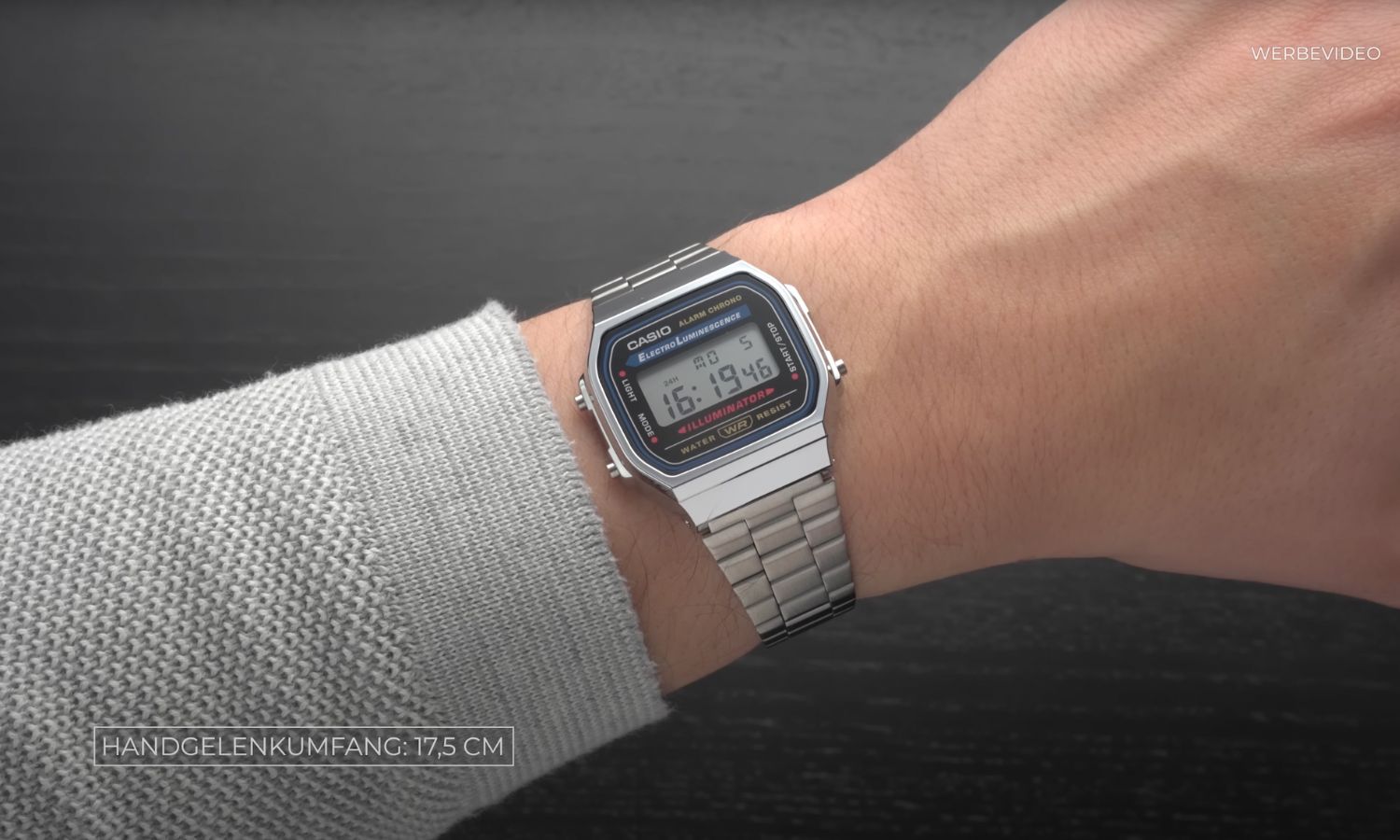 Casio A168 am Edelstahlarmband an einem Handgelenk mit hellgrauem Ärmel getragen vor schwarzem Hintergrund