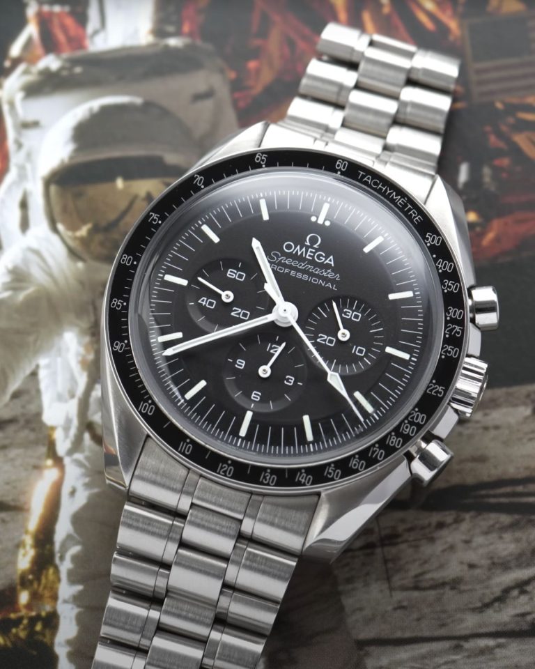OMEGA Speedmaster Moonwatch Hesalit mit schwarzem Zifferblatt am Edelstahlarmband liegend vor dem Bild eines Astronauten