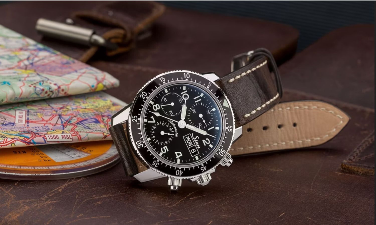 Sinn 103 St Sa mit schwarzem Zifferblatt am braunen Lederarmband auf der Seite liegend vor braunem Hintergrund