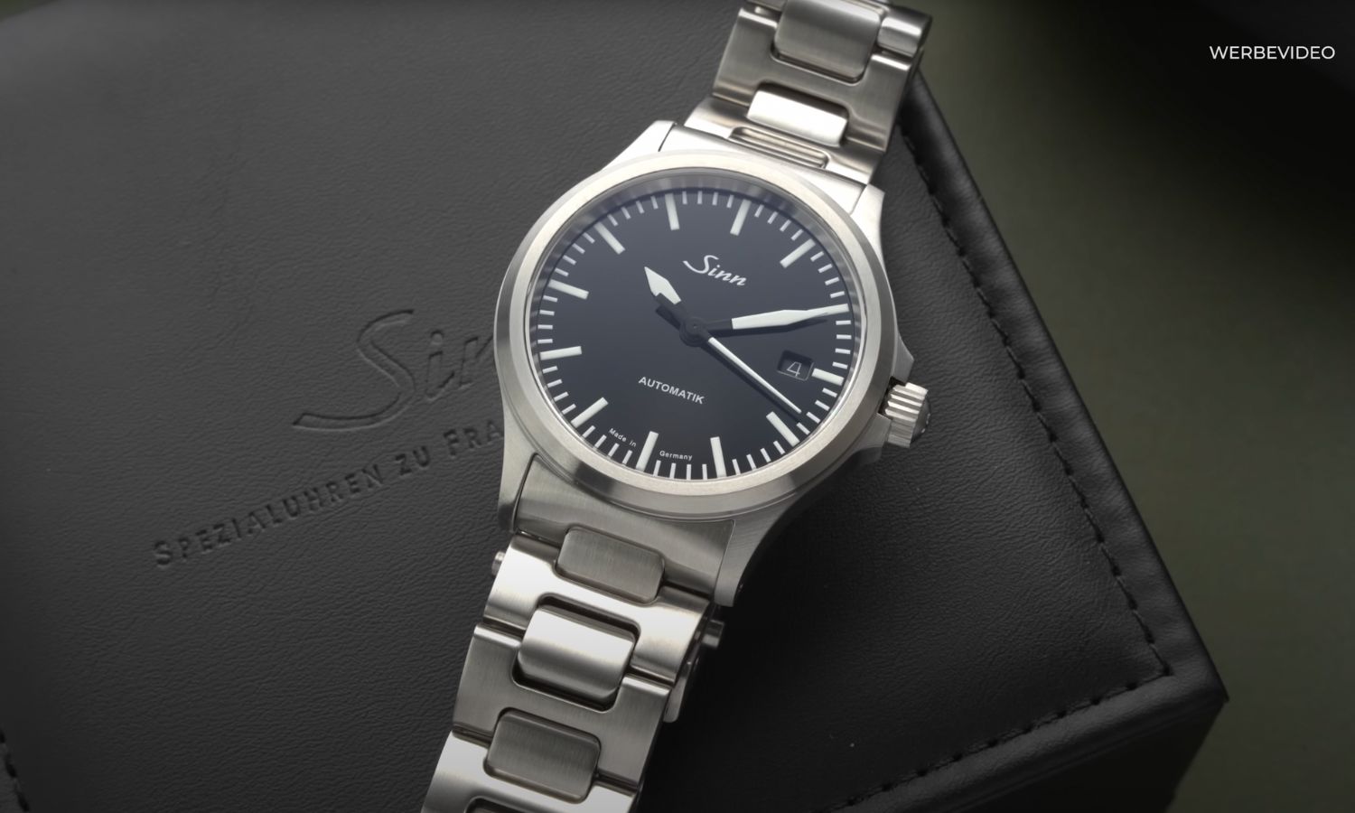Sinn 556 mit schwarzem Zifferblatt am Edelstahlarmband liegend vor schwarzem Hintergrund