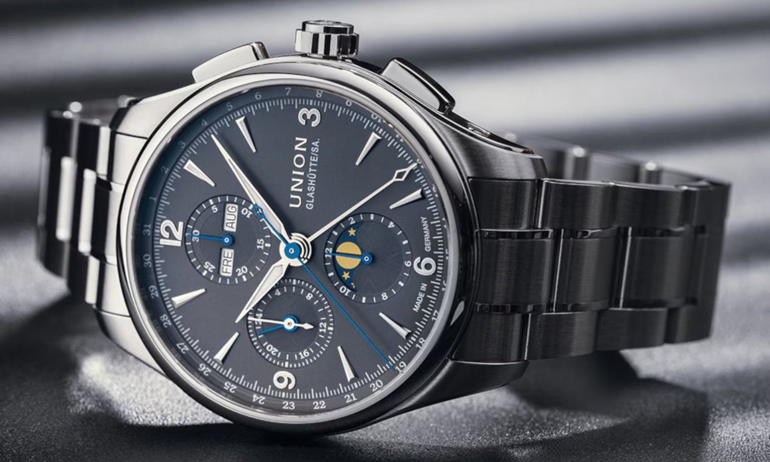 Union Glashütte Belisar Chronograph Moon Phase mit grauem Zifferblatt am Edelstahlarmband auf der Seite liegend vor grauem Hintergrund