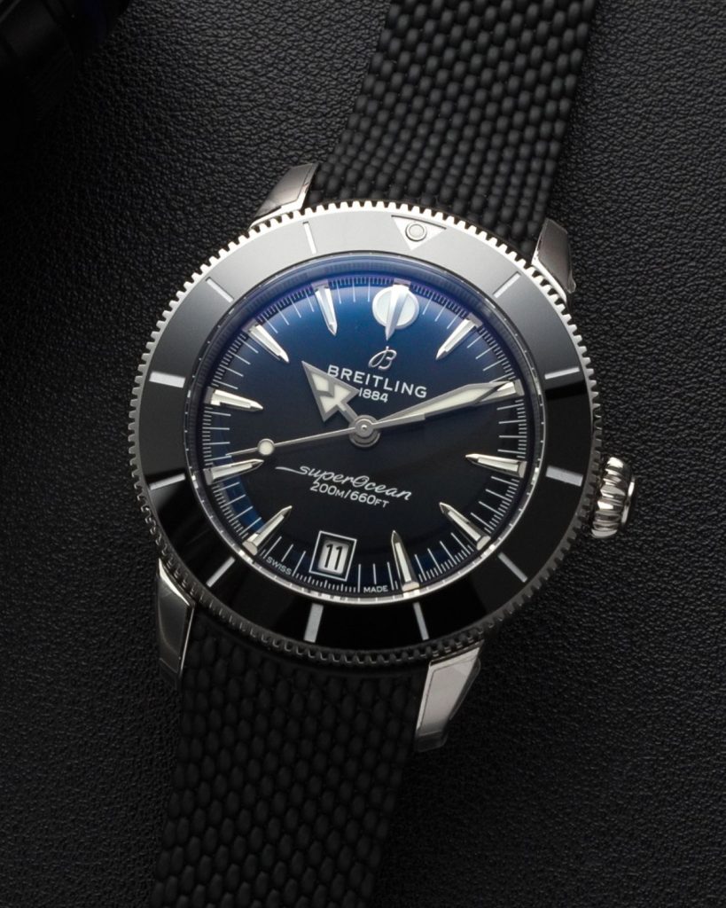 Breitling Superocean Heritage B31 Automatic 40 mit schwarzem Zifferblatt am schwarzen Kautschukarmband liegend vor schwarzem Hintergrund