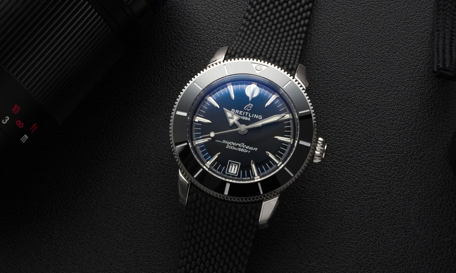 Breitling Superocean Heritage B31 Automatic 40 mit schwarzem Zifferblatt am schwarzen Kautschukarmband liegend vor schwarzem Hintergrund