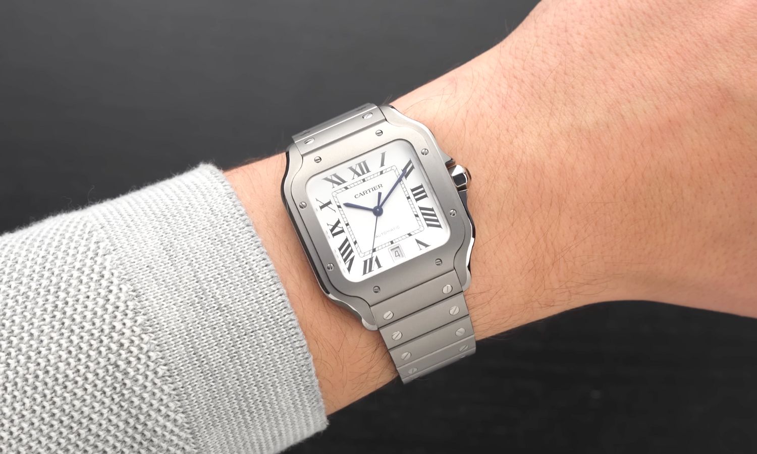 Cartier Santos de Cartier Titan Referenz WSSA0089 mit weißem Zifferblatt am Titanarmband an einem Handgelenk mit hellgrauem Ärmel getragen vor schwarzem Hintergrund
