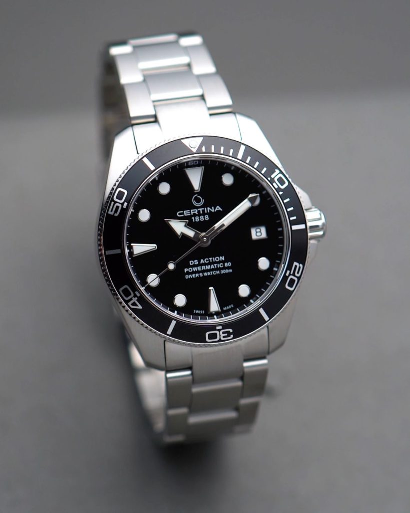 Certina DS Action Diver 38mm mit schwarzem Zifferblatt am Edelstahlarmband stehend vor grauem Hintergrund