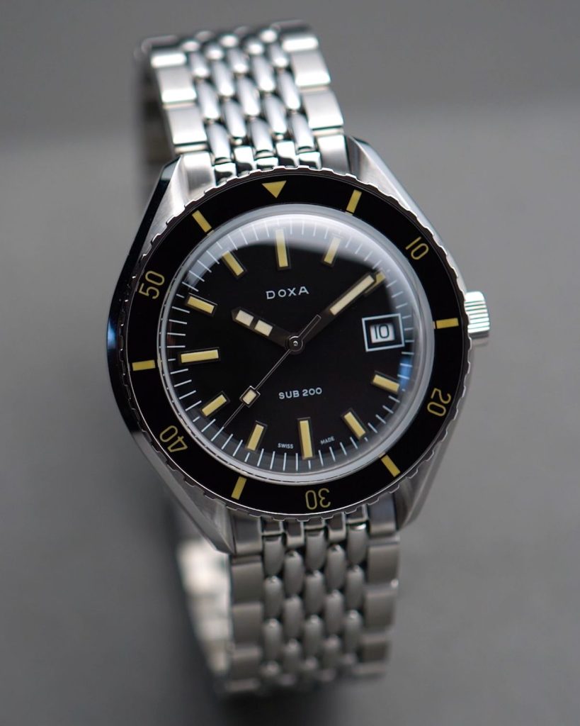 Doxa Sub 200T Sharkhunter mit schwarzem Zifferblatt am Edelstahlarmband stehend vor grauem Hintergrund