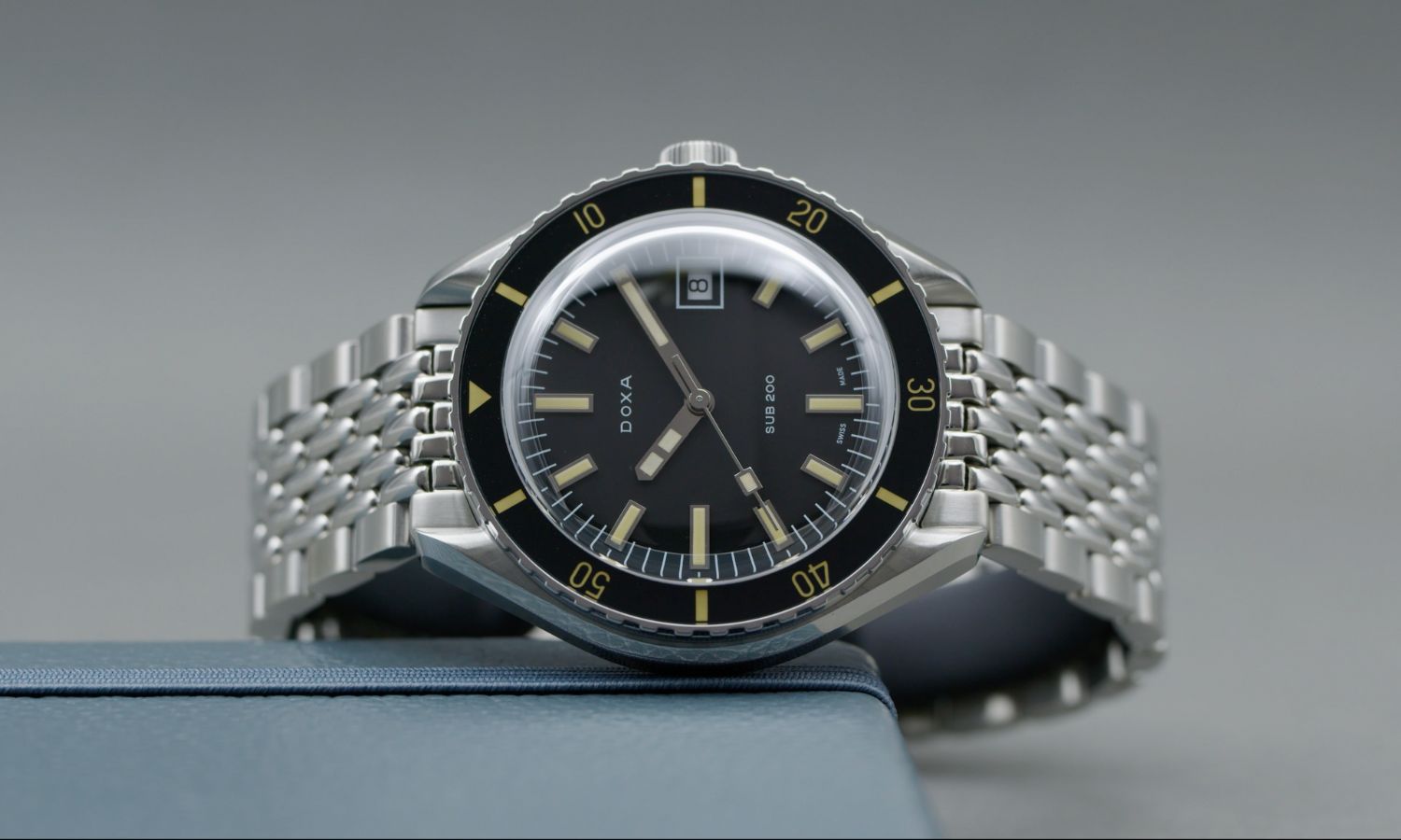 Doxa Sub 200T Sharkhunter mit schwarzem Zifferblatt am Edelstahlarmband seitlich liegend vor grauem Hintergrund