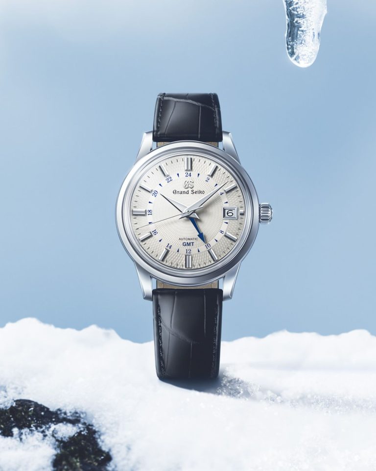 Grand Seiko SBGM255 „Snowdrop“ mit weißem Zifferblatt am dunkelblauen Lederarmband stehend von vorne abgebildet vor blau-weißem Hintergrund