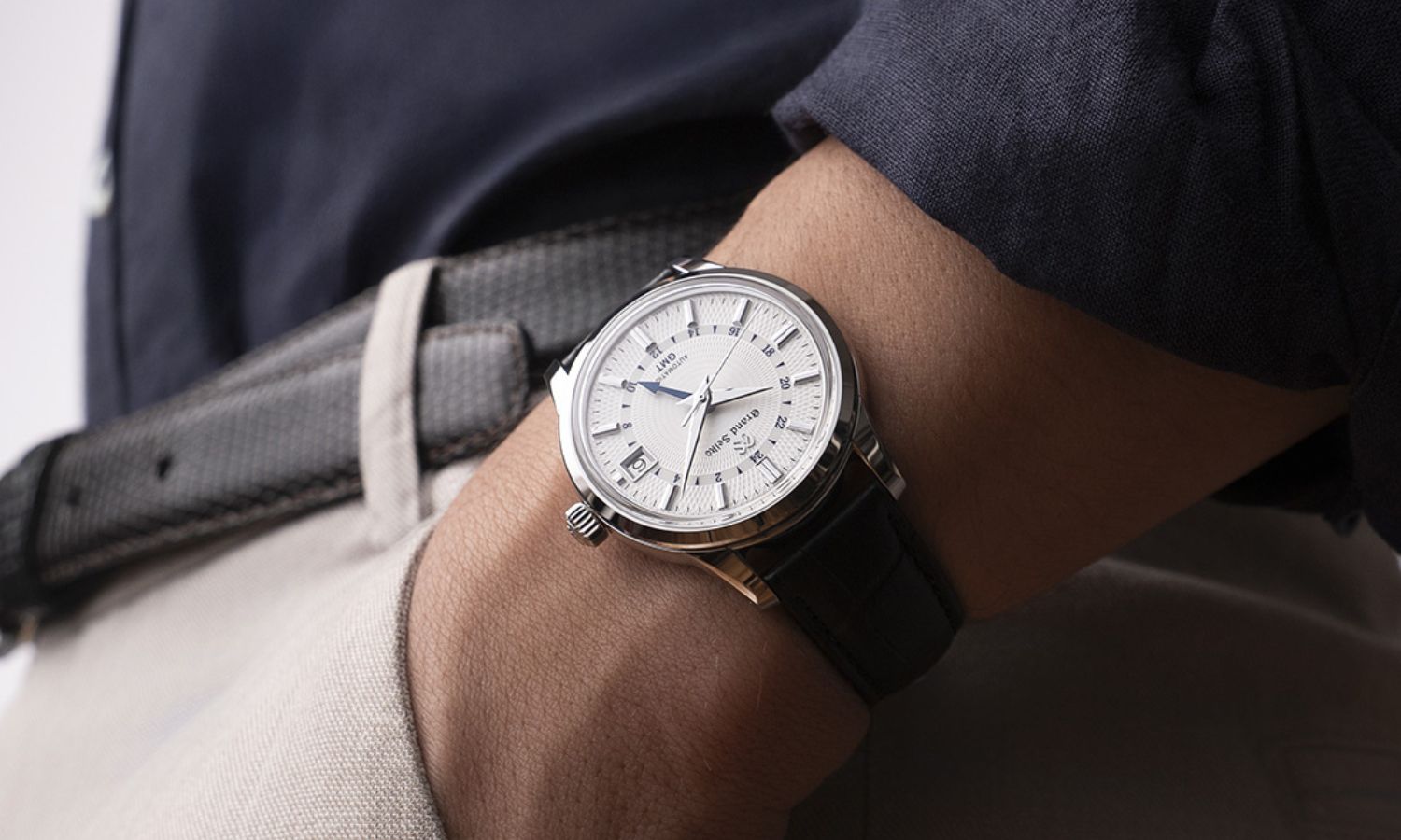Grand Seiko SBGM255 „Snowdrop“ mit weißem Zifferblatt am dunkelblauen Lederarmband an einem Handgelenk mit dunkelblauem Ärmel getragen mit der Hand in der Hosentasche