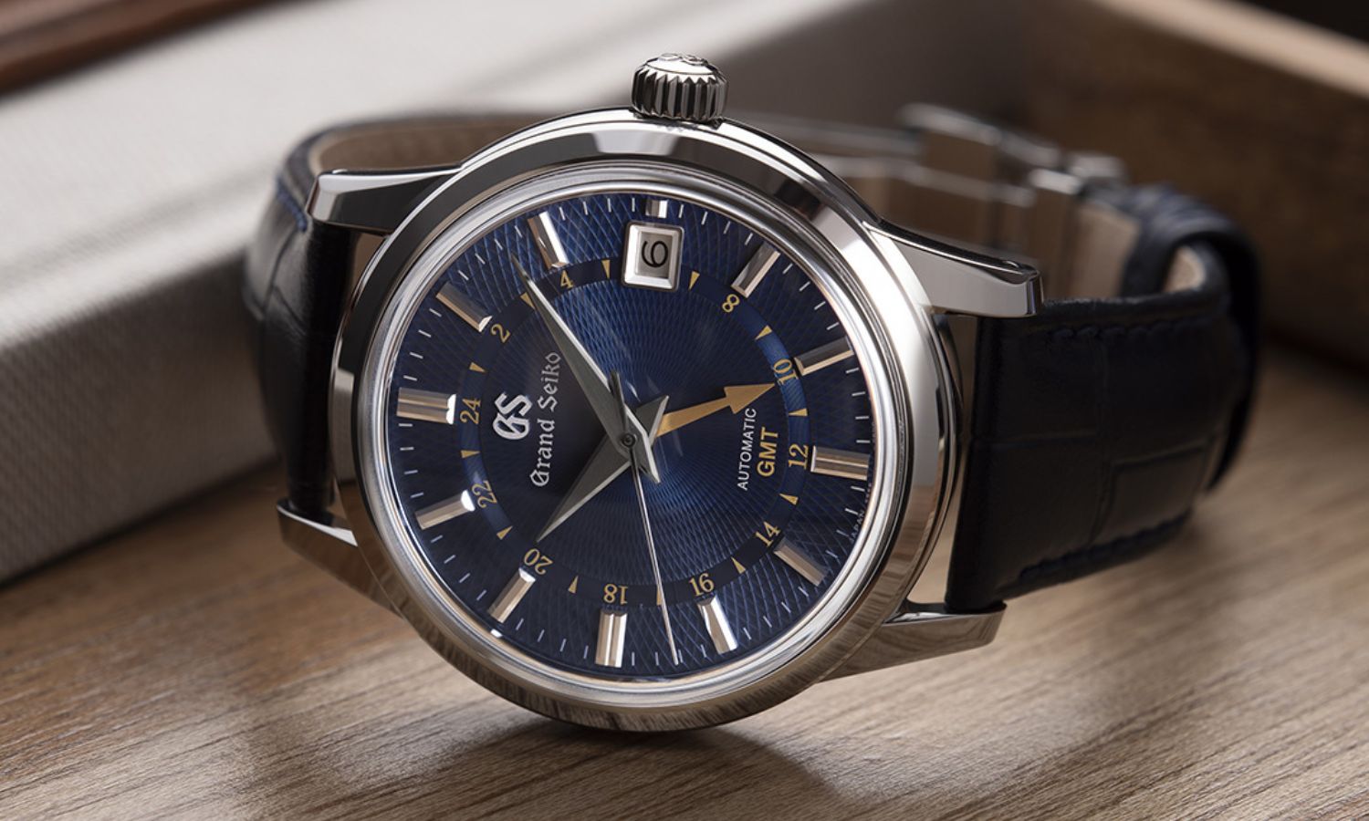 Grand Seiko SBGM257 „Moondrop“ mit dunkelblauem Zifferblatt am dunkelblauen Lederarmband seitlich liegend von vorne abgebildet vor hölzernem Hintergrund