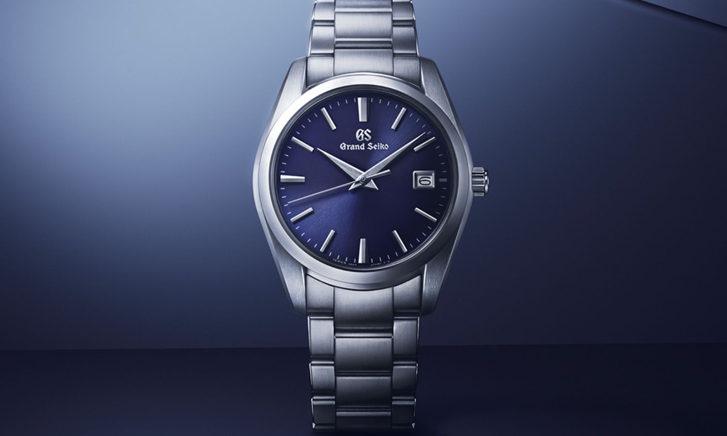 Grand Seiko SBGX265 mit dunkelblauem Zifferblatt am Edelstahlarmband stehend von vorne abgebildet vor dunkelblauem Hintergrund