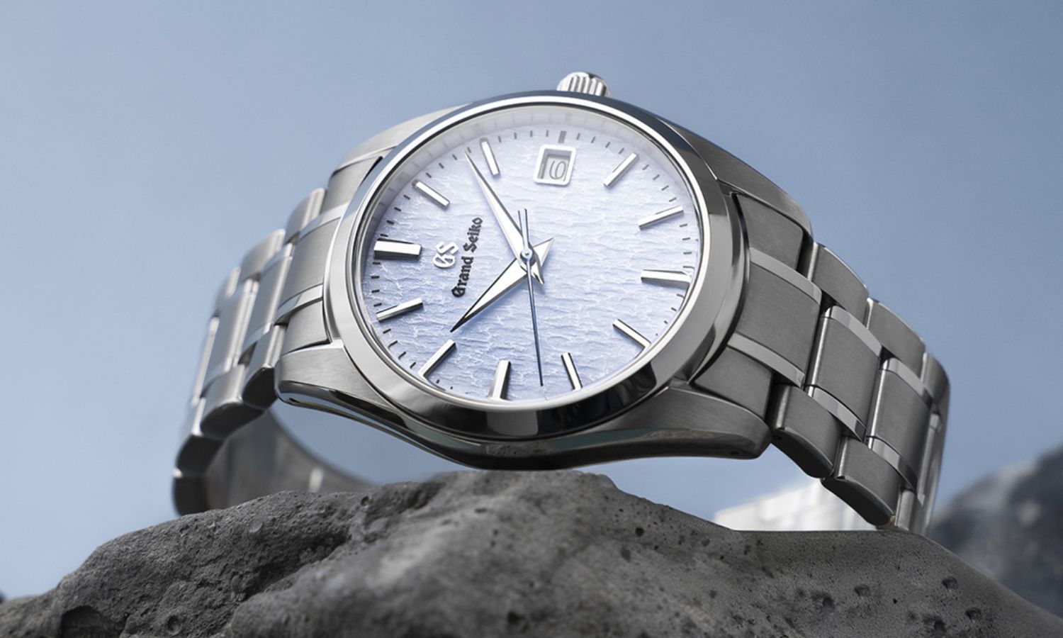 Grand Seiko SBGX357 Skyflake mit hellblauem Zifferblatt am Edelstahlarmband seitlich liegend von vorne abgebildet vor hellblauem Hintergrund
