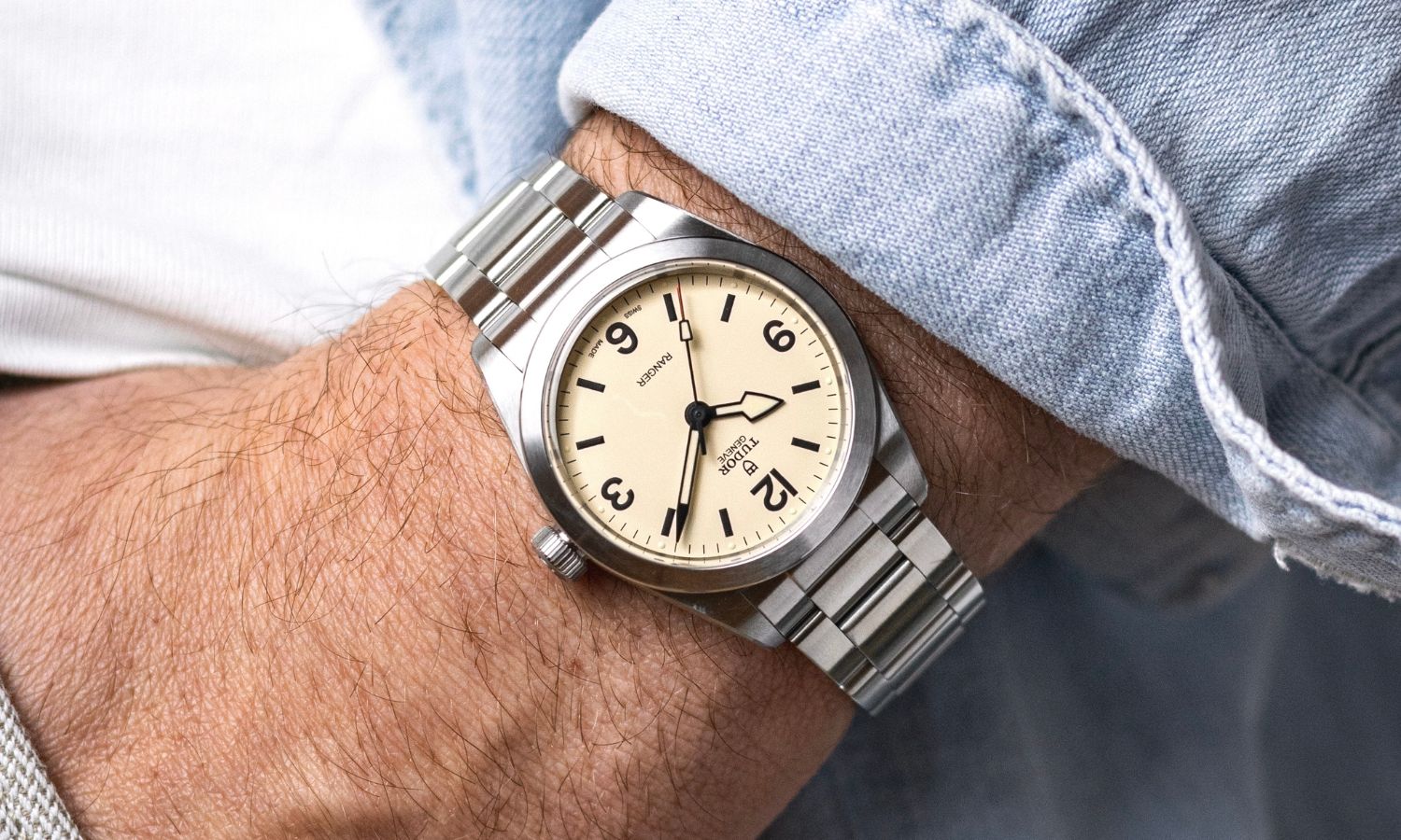 TUDOR Ranger „Dune White“ mit cremeweißem Zifferblatt am Edelstahlarmband an einem Handgelenk mit hellblauem Ärmel getragen mit der Hand in der Hosentasche