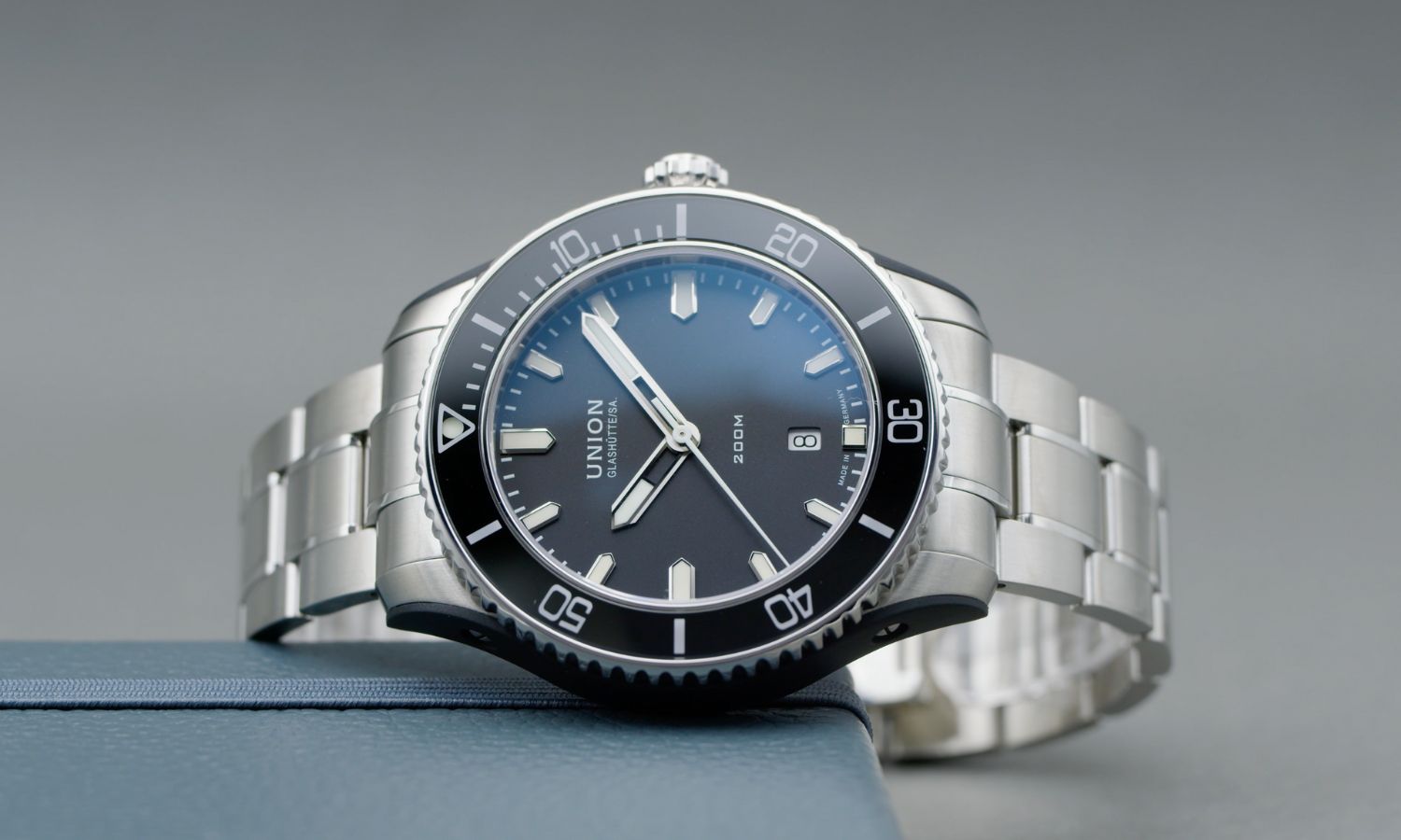 UNION Glashütte Belisar Datum Sport mit schwarzem Zifferblatt am Stahlband seitlich liegend vor grauem Hintergrund