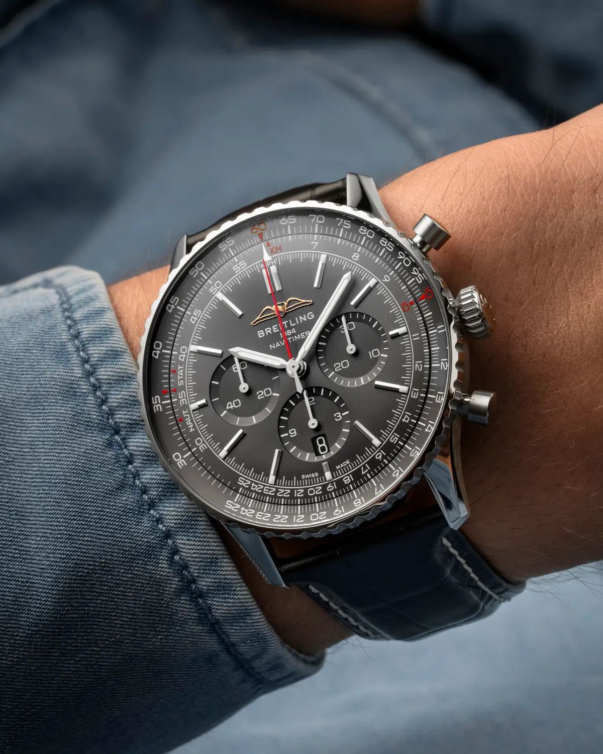 Breitling Navitimer Germany Edition mit anthrazitfarbenem Zifferblatt am schwarzen Lederarmband an einem Handgelenk mit blauem Ärmel getragen