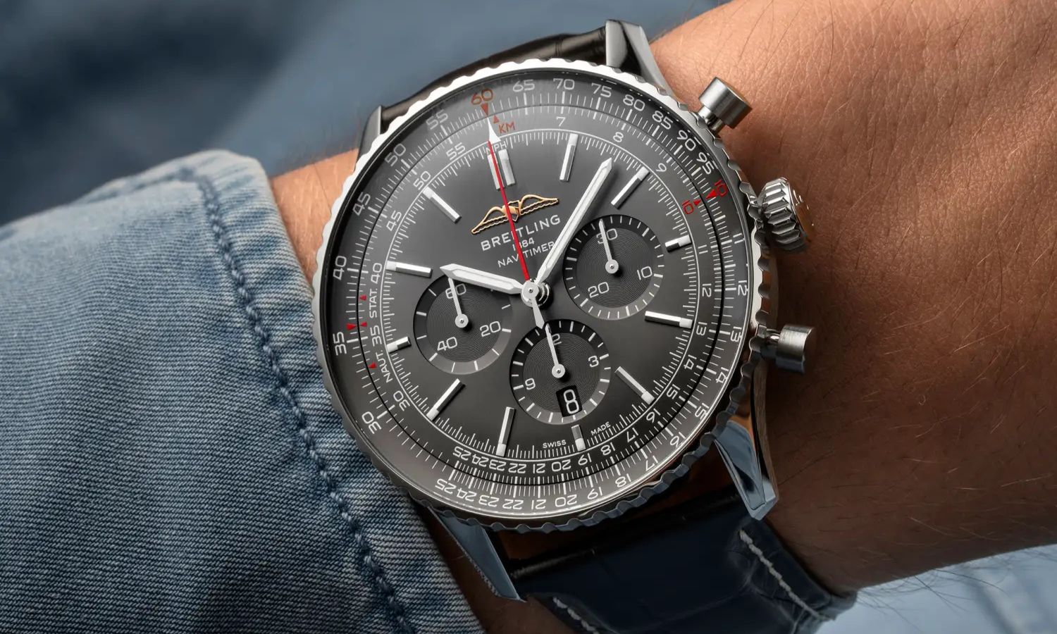 Breitling Navitimer Germany Edition mit anthrazitfarbenem Zifferblatt am schwarzen Lederarmband an einem Handgelenk mit blauem Ärmel getragen