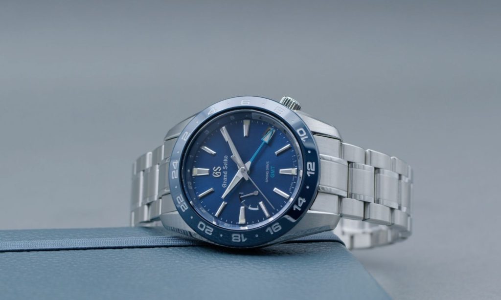 Grand Seiko Sport Spring Drive SBGE255 mit blauem Zifferblatt am Edelstahlarmband seitlich liegend vor hellgrauem Hintergrund abgebildet