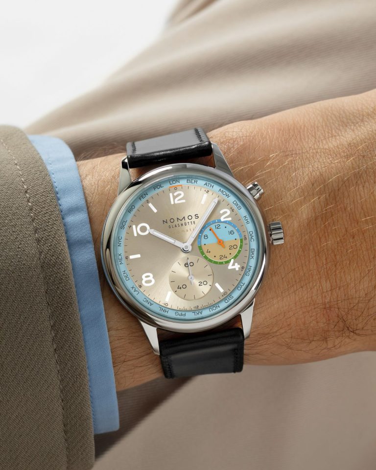 NOMOS Glashütte Club Sport neomatik Weltzeit Roam (Ref. 790.S10) mit champagnerfarbenem Zifferblatt am schwarzen Lederarmband an einem Handgelenk mit beigem Ärmel getragen