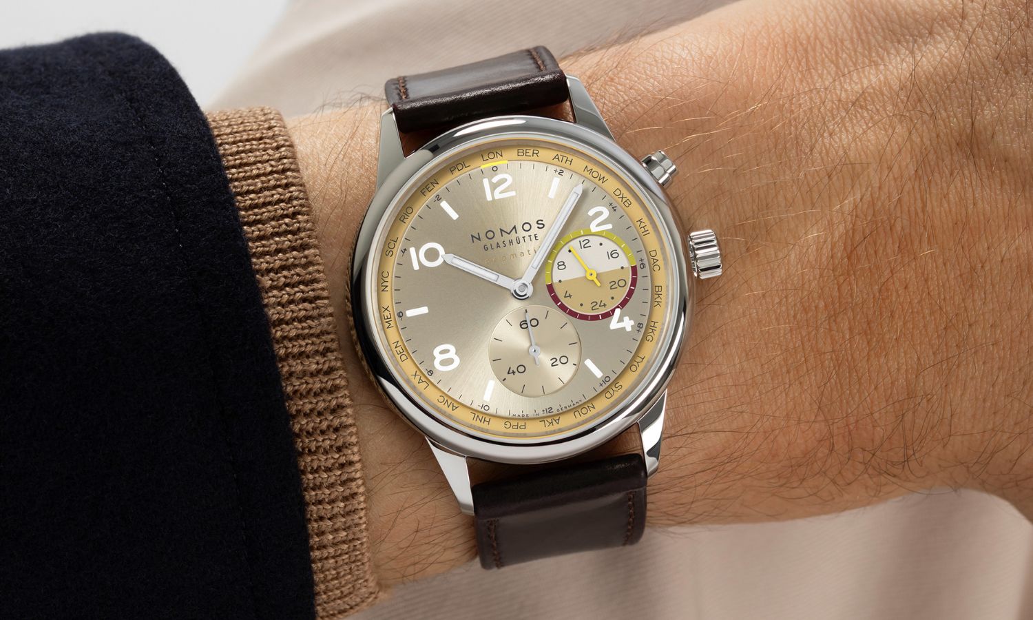 NOMOS Glashütte Club Sport neomatik Weltzeit Reverie (Ref. 790.S11) mit champagnerfarbenem Zifferblatt am braunen Lederarmband an einem Handgelenk mit schwarzem Ärmel getragen