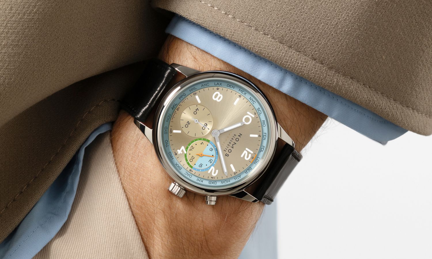 NOMOS Glashütte Club Sport neomatik Weltzeit Roam (Ref. 790.S10) mit champagnerfarbenem Zifferblatt am schwarzen Lederarmband an einem Handgelenk mit beigem Ärmel getragen